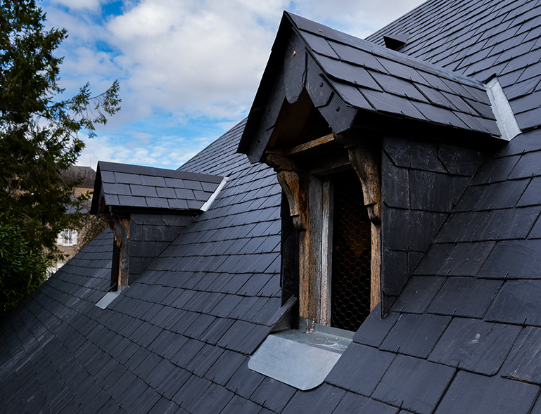 détail couverture toiture en ardoise avec lucarnes bois anciennes sur bâtisse de montagne