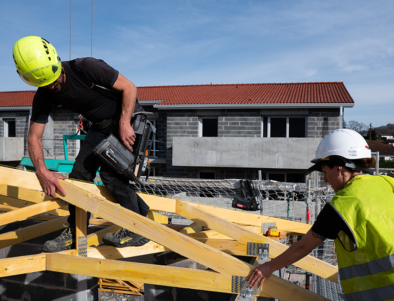 deux charpentiers posant des fermes de charpente bois à la cloueuse sur chantier de construction neuve