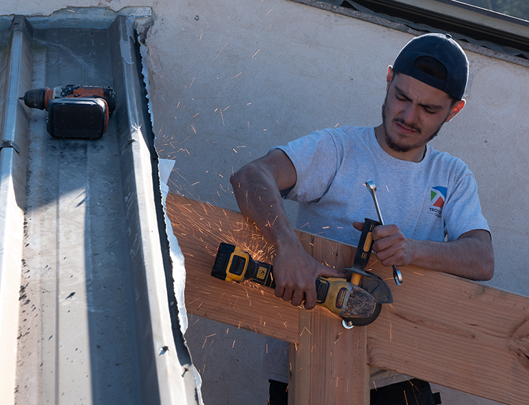 charpentier Troyano Charpente découpant une pièce métallique à la meuleuse avec des étincelles sur chantier