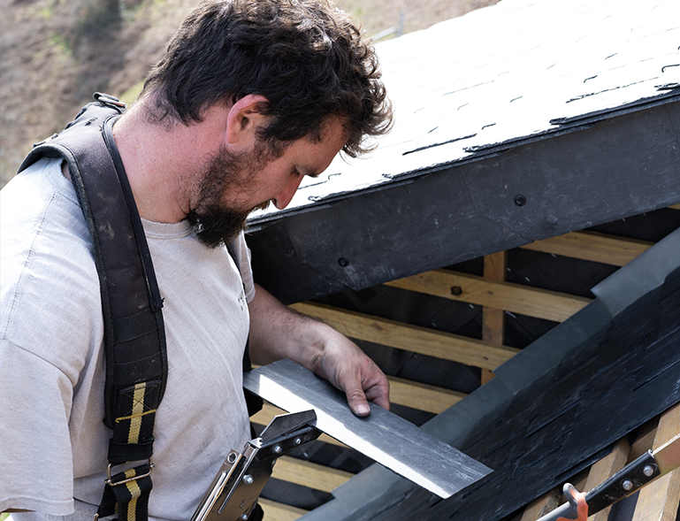 couvreur posant des ardoises à la main avec soin sur chantier de toiture