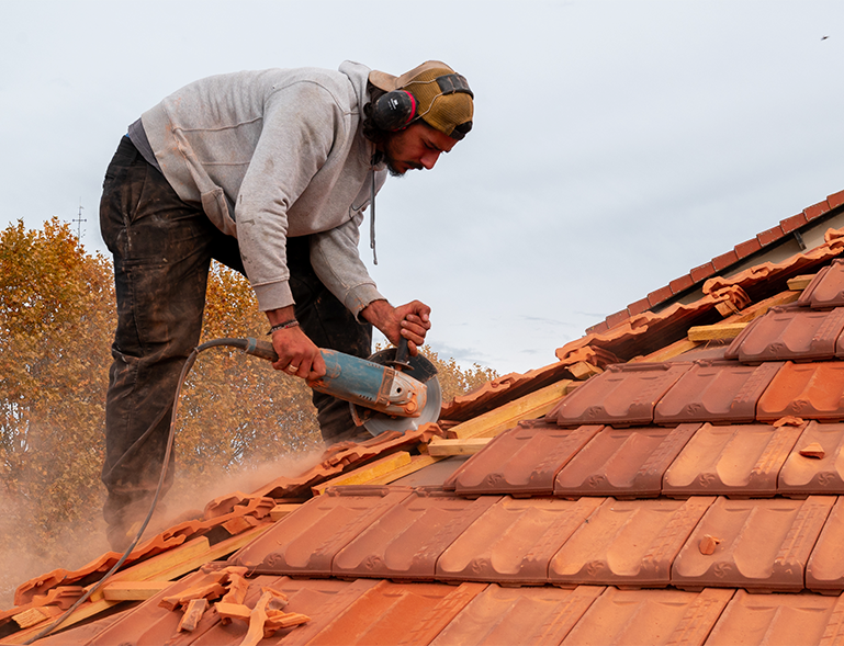 couvreur découpant une tuile rouge à la meuleuse sur chantier de réfection de toiture