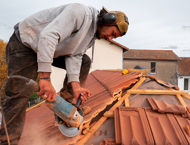couvreur découpant une tuile rouge à la meuleuse sur chantier de réfection de toiture
