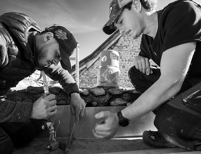 deux zingueurs façonnant et soudant un solin zinc au chalumeau sur chantier de rénovation toiture en pierre