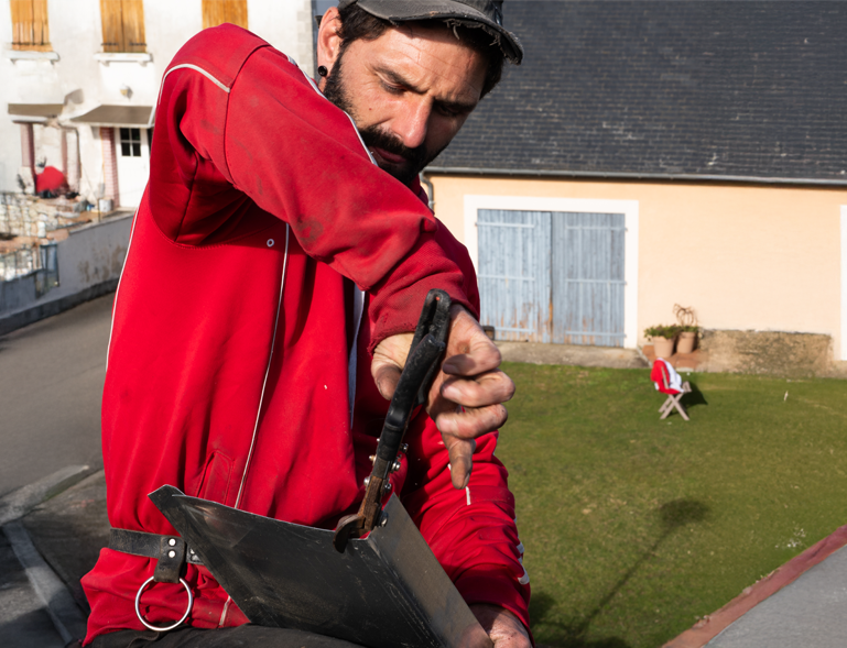 couvreur façonnant une pièce de zinc à la pince sur chantier de toiture en ardoise