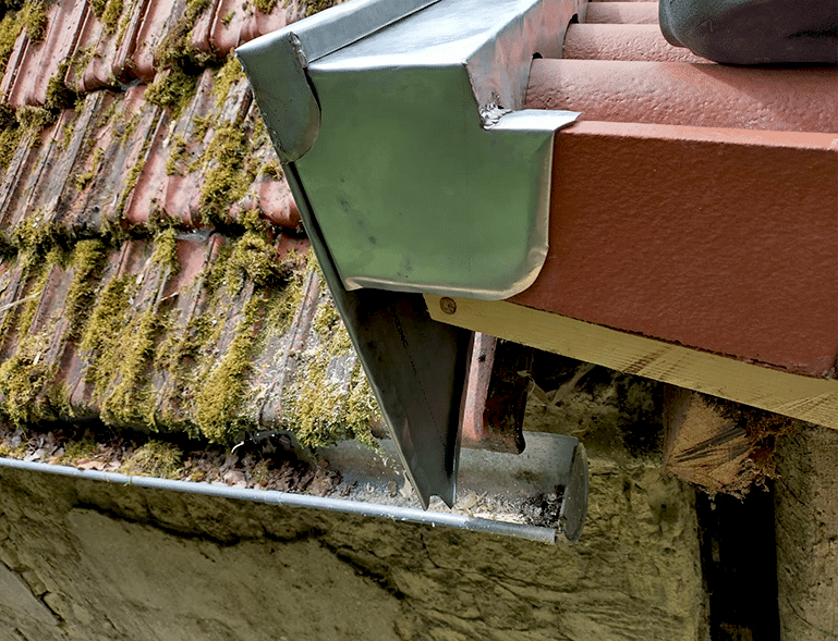 Gros plan d’une gouttière en métal fixée sur une planche de rive en bois, bordée de tuiles rouges