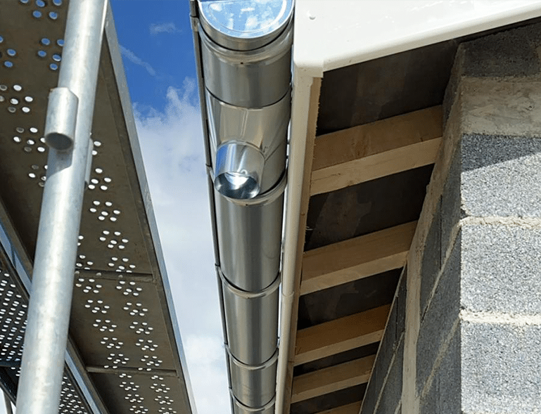 Gouttière métallique neuve avec raccord de descente, fixée à une planche de rive blanche et des poutres en bois.