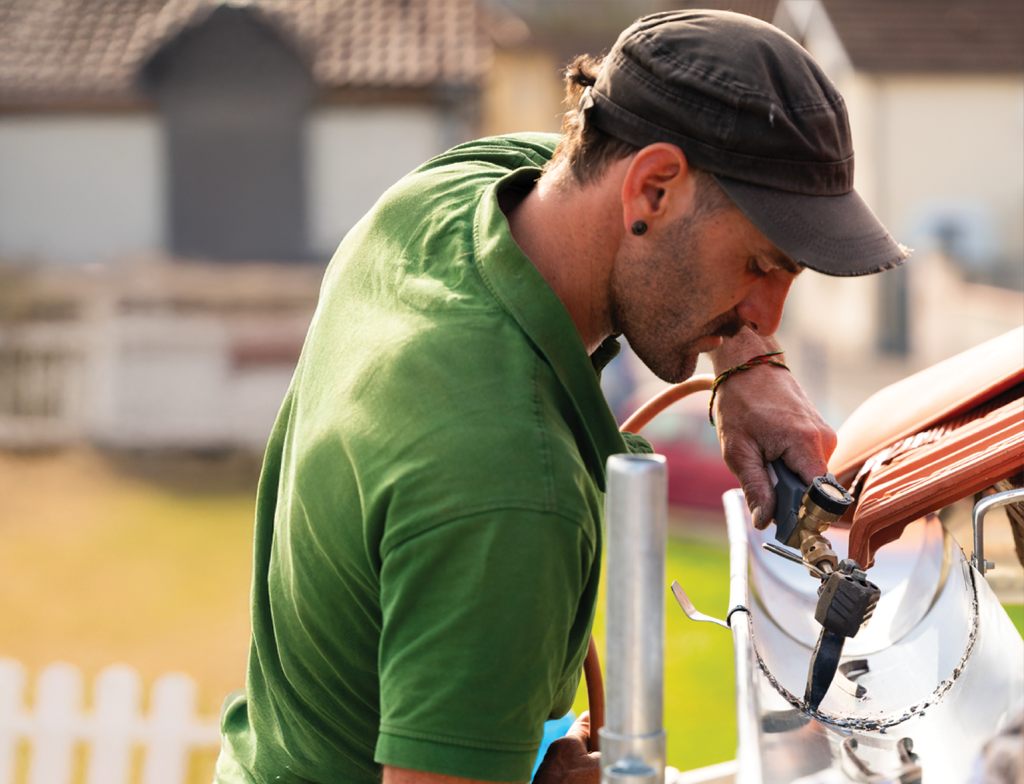 couvreur soudant au chalumeau une gouttière zinc sur rive de toiture en tuile rouge